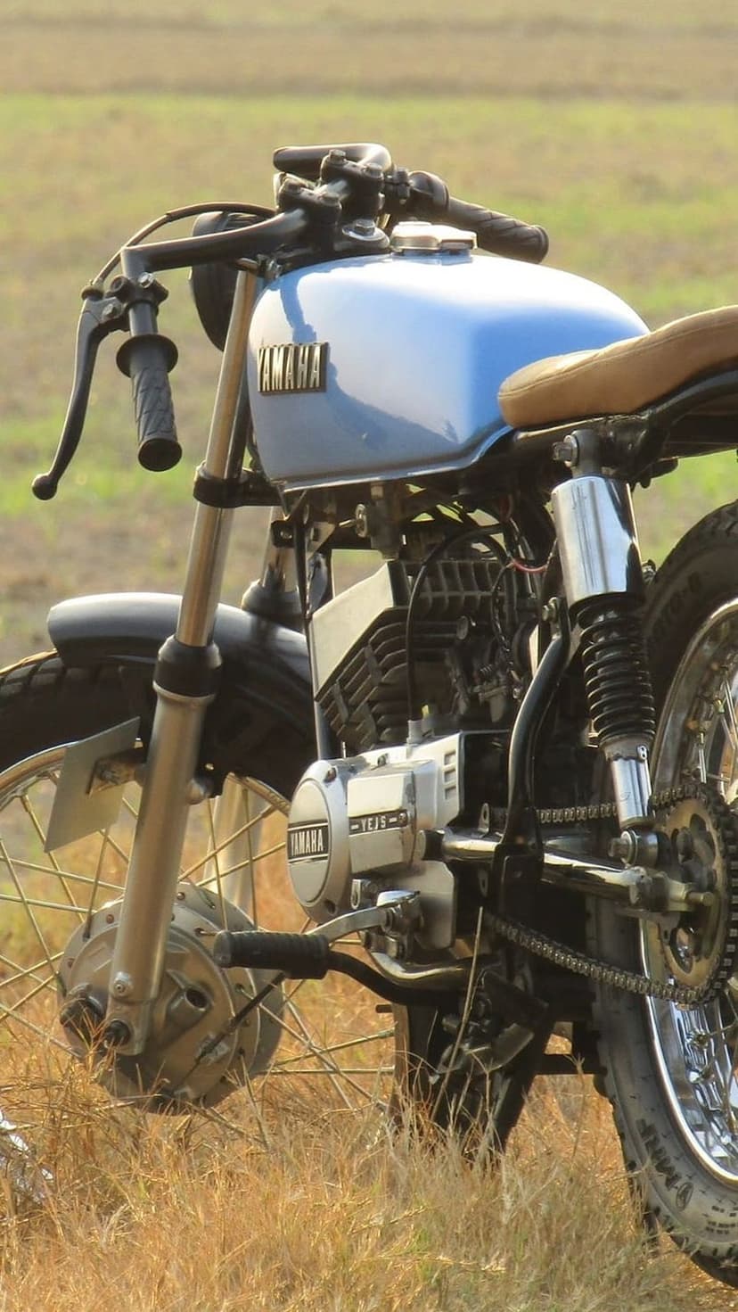 Blue Yamaha cafe racer motorcycle featuring a brown leather seat and polished chrome engine in a soft field.