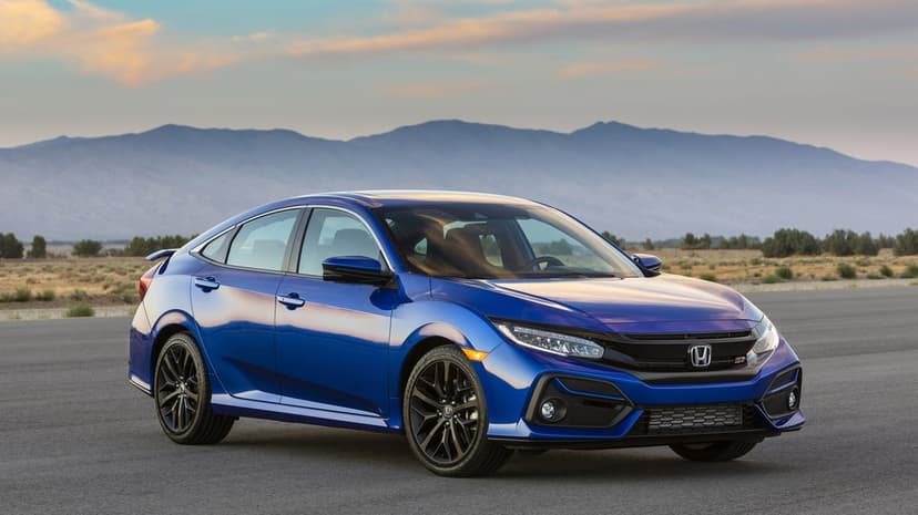 Blue Honda Civic Si sedan on asphalt with a mountain backdrop under a soft orange and blue sunset sky.
