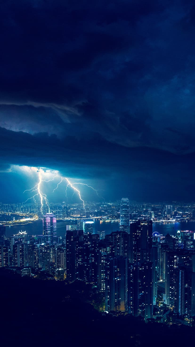Vertical lightning bolts flash over a luminous metropolitan skyline and dark coastal waters at night.