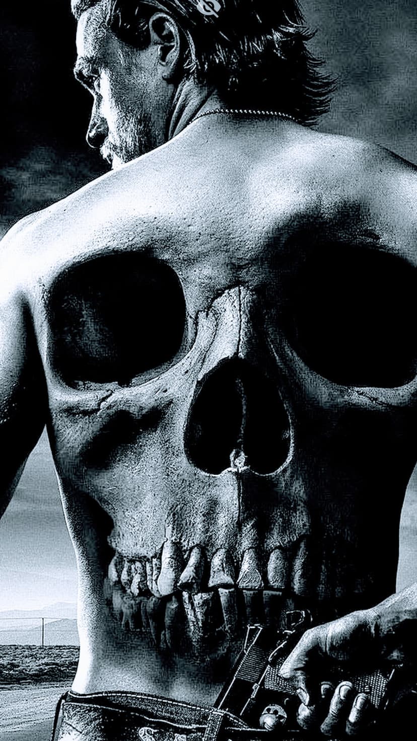 Man with a detailed skull back tattoo holds a handgun while facing a desolate monochrome desert landscape.