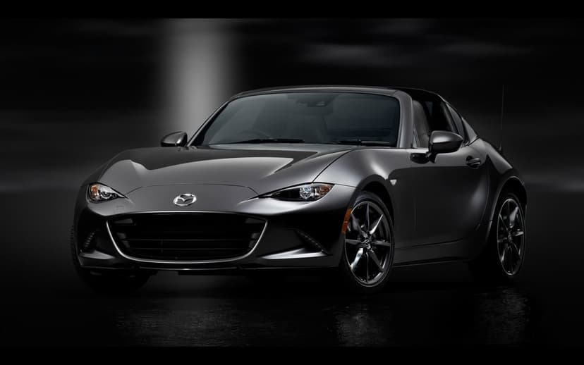 Metallic gray Mazda MX-5 RF sports car in a dark studio with dramatic lighting and floor reflections.