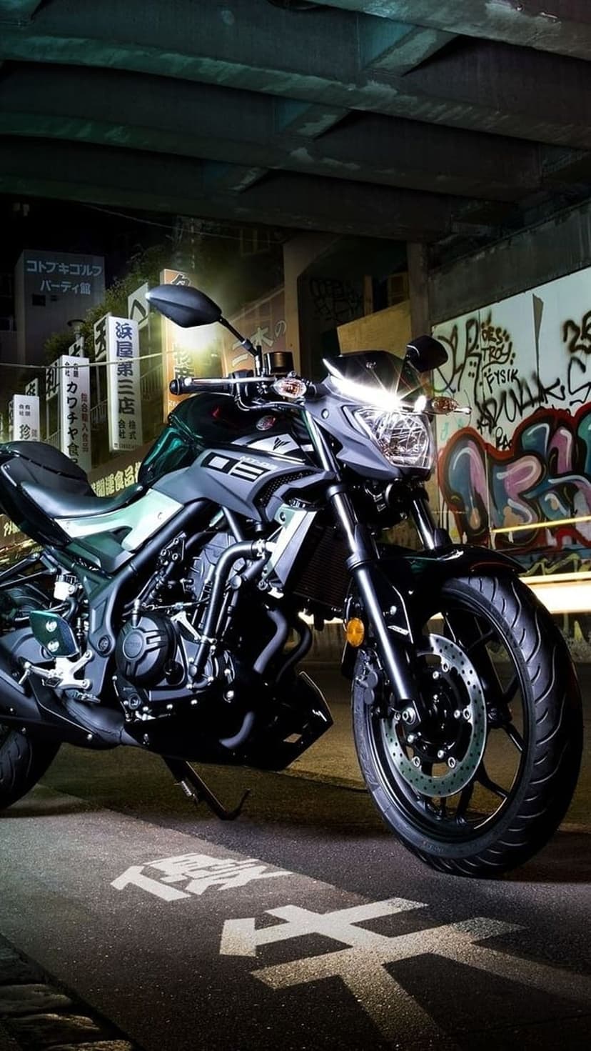 Black sportbike parked on a dark street in front of colorful graffiti and glowing Japanese neon signage at night.