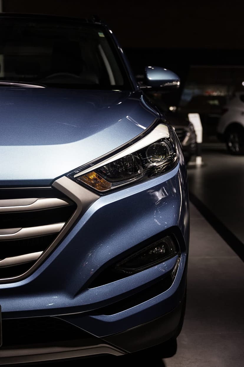 Metallic blue Hyundai Tucson headlight and dark grille featuring chrome accents and sharp LED lighting elements.