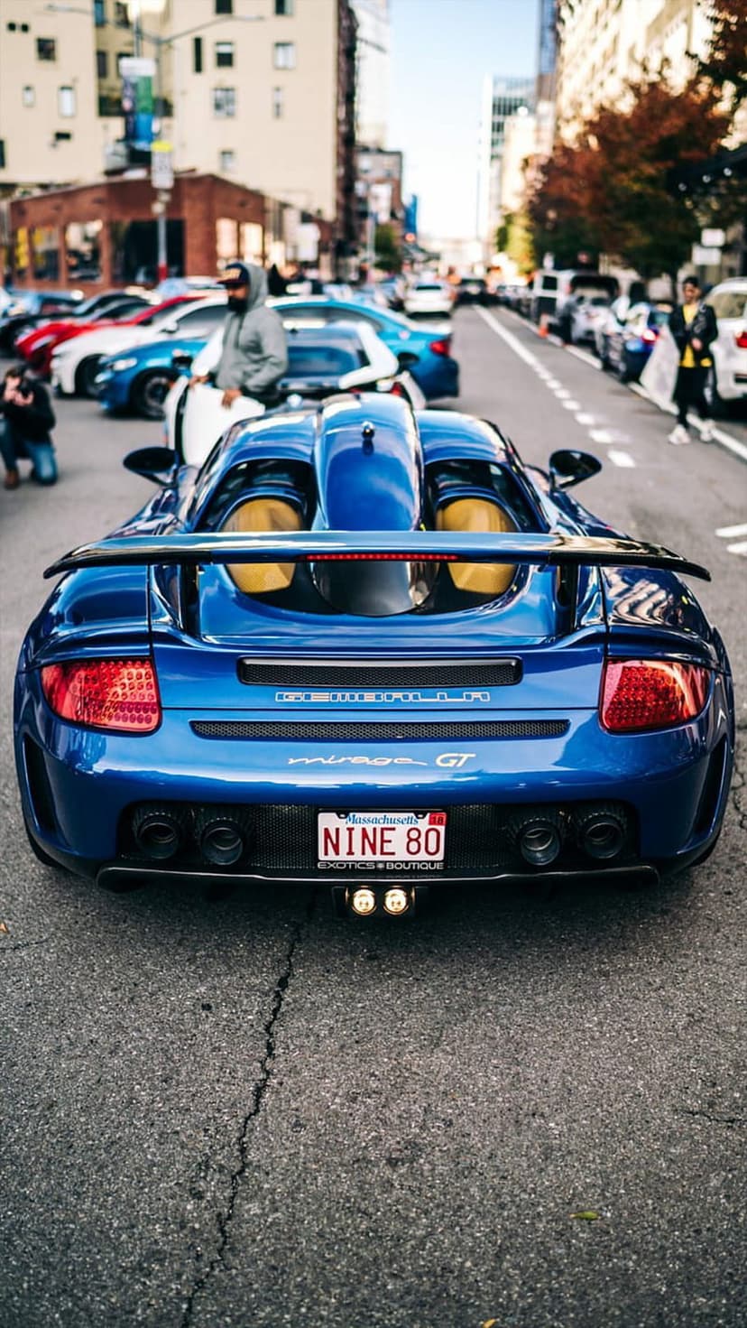 Blue Porsche Mirage GT supercar with a large rear spoiler and Massachusetts license plate on a city street.