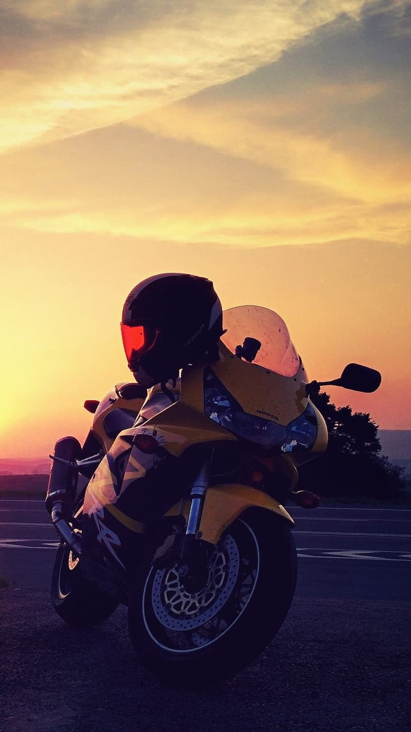 Yellow sport motorcycle and black helmet on a roadside under an orange sunset sky during the golden hour.