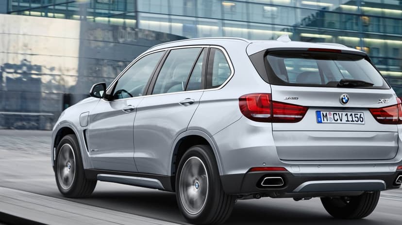 Silver BMW X5 luxury SUV in motion past a glass building with spinning wheels and sleek metallic reflections.