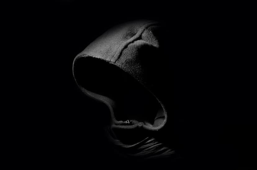 Hoodie silhouette with high-contrast shadows and visible fabric texture against a dark, minimalist background.