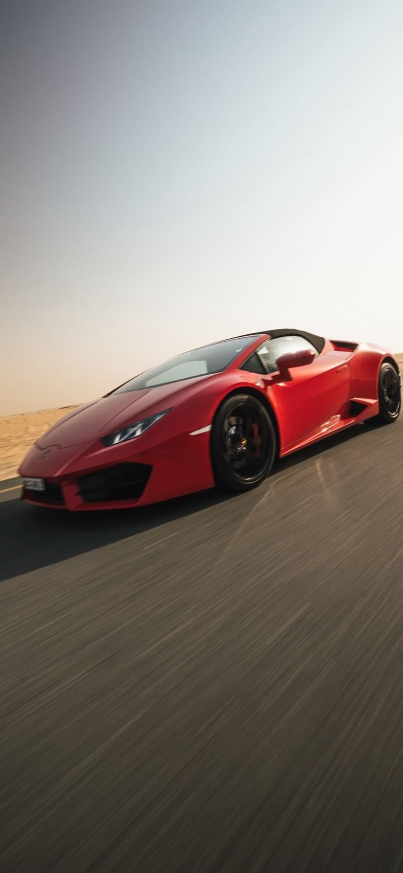 Red Lamborghini convertible speeding on a desert road with motion blur under a clear blue sky in daylight.