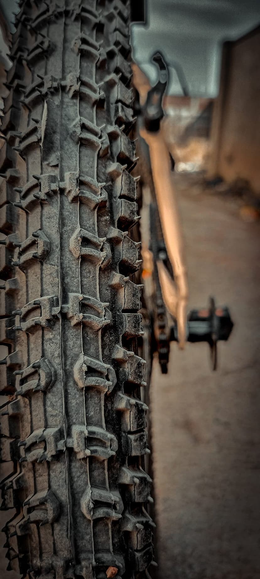 Black rubber mountain bike tire treads with deep grooves and a blurred pedal background for mobile display.