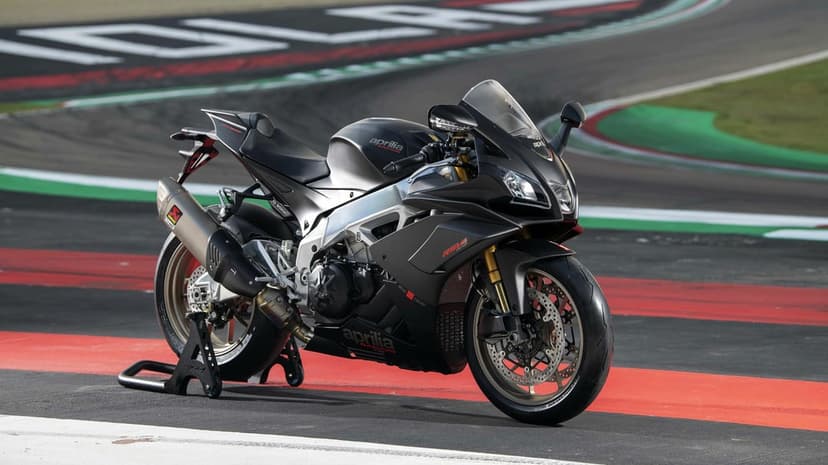 Matte black Aprilia RSV4 Factory superbike with carbon fiber accents parked on a professional racetrack.