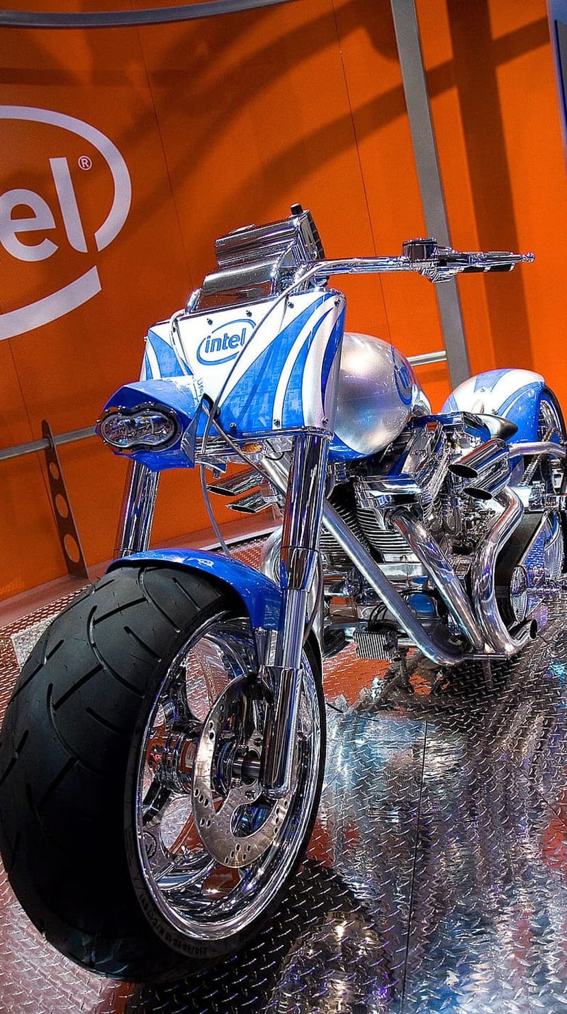 Intel custom motorcycle with blue paint and chrome accents stands before an orange logo on a vertical screen.