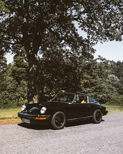 Classic Black Porsche 911 parked under a large oak tree