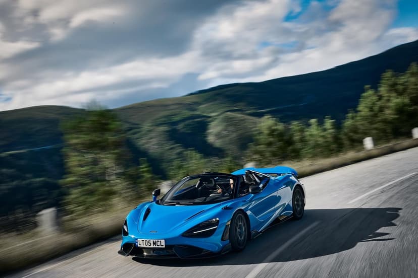 Blue convertible supercar driving fast on a winding mountain road with green hills and cloudy sky behind.