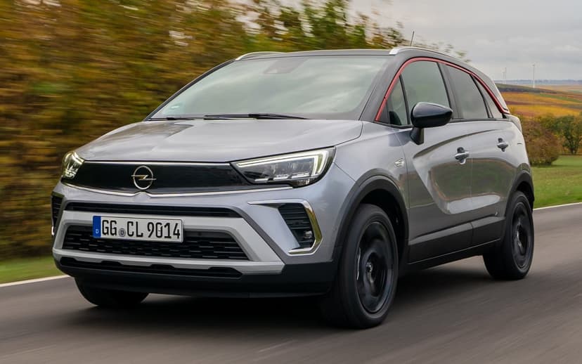 Silver Opel Crossland SUV driving on an asphalt road with motion-blurred trees and a distinct red roof accent line.
