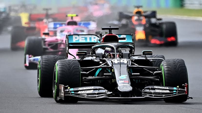 Black Mercedes F1 car with teal accents leading a pack of racing cars on a wet track with tire spray.