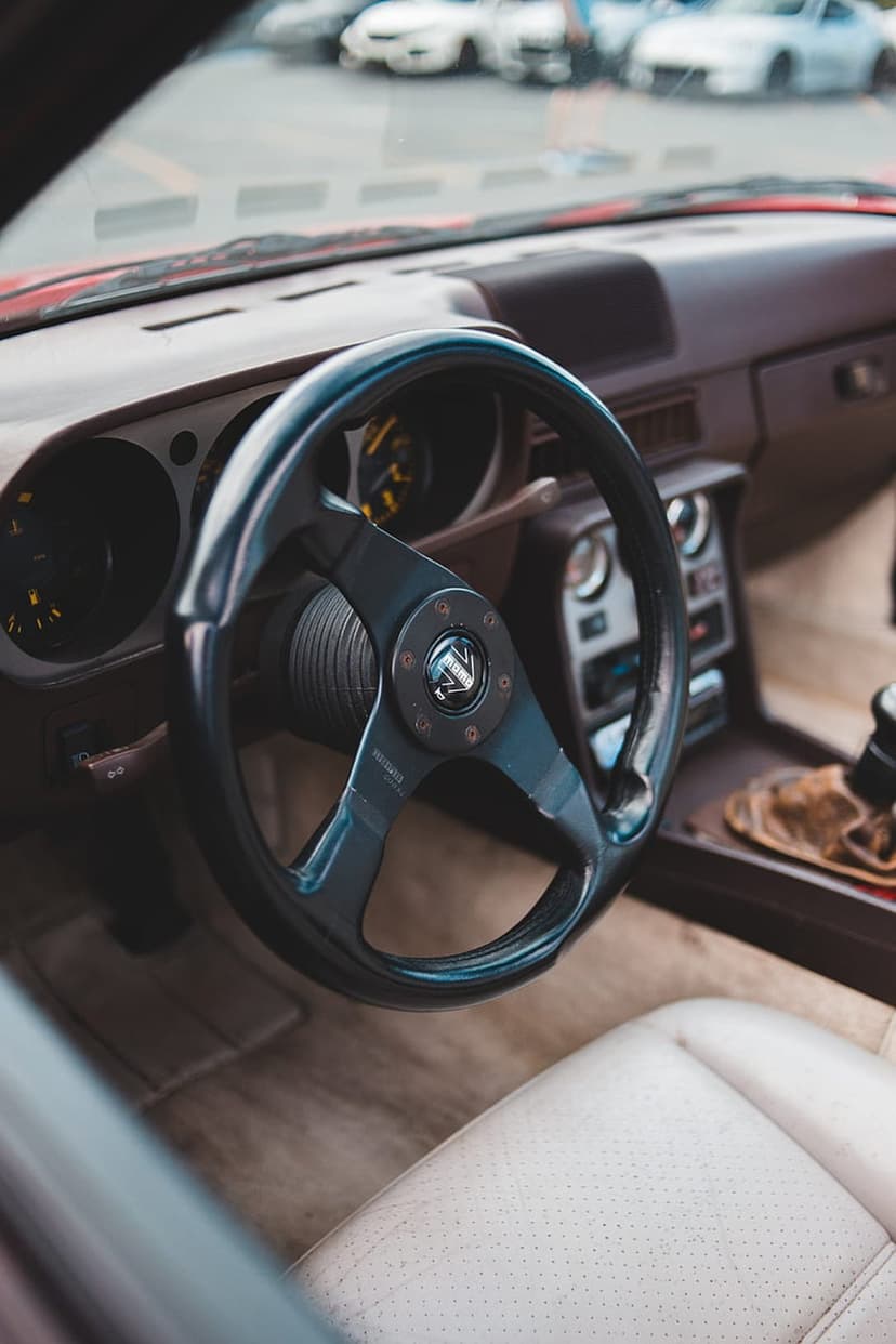 Vintage car steering wheel and dashboard featuring perforated leather seats and a gear shifter in soft light.