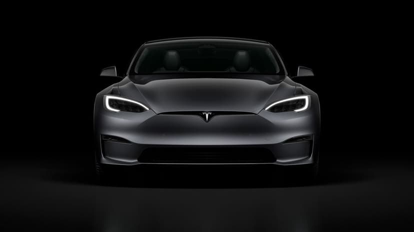 Front view of a dark grey Tesla with glowing LED headlights centered against a solid black background.
