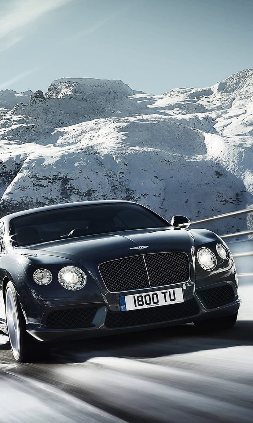 Dark Bentley Continental GT driving on a winding snowy road with icy mountain peaks under a clear blue sky.