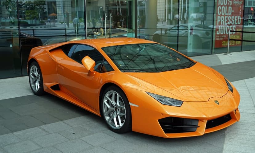 Orange Lamborghini Huracan parked on a stone walkway in front of a modern glass office building at daytime.