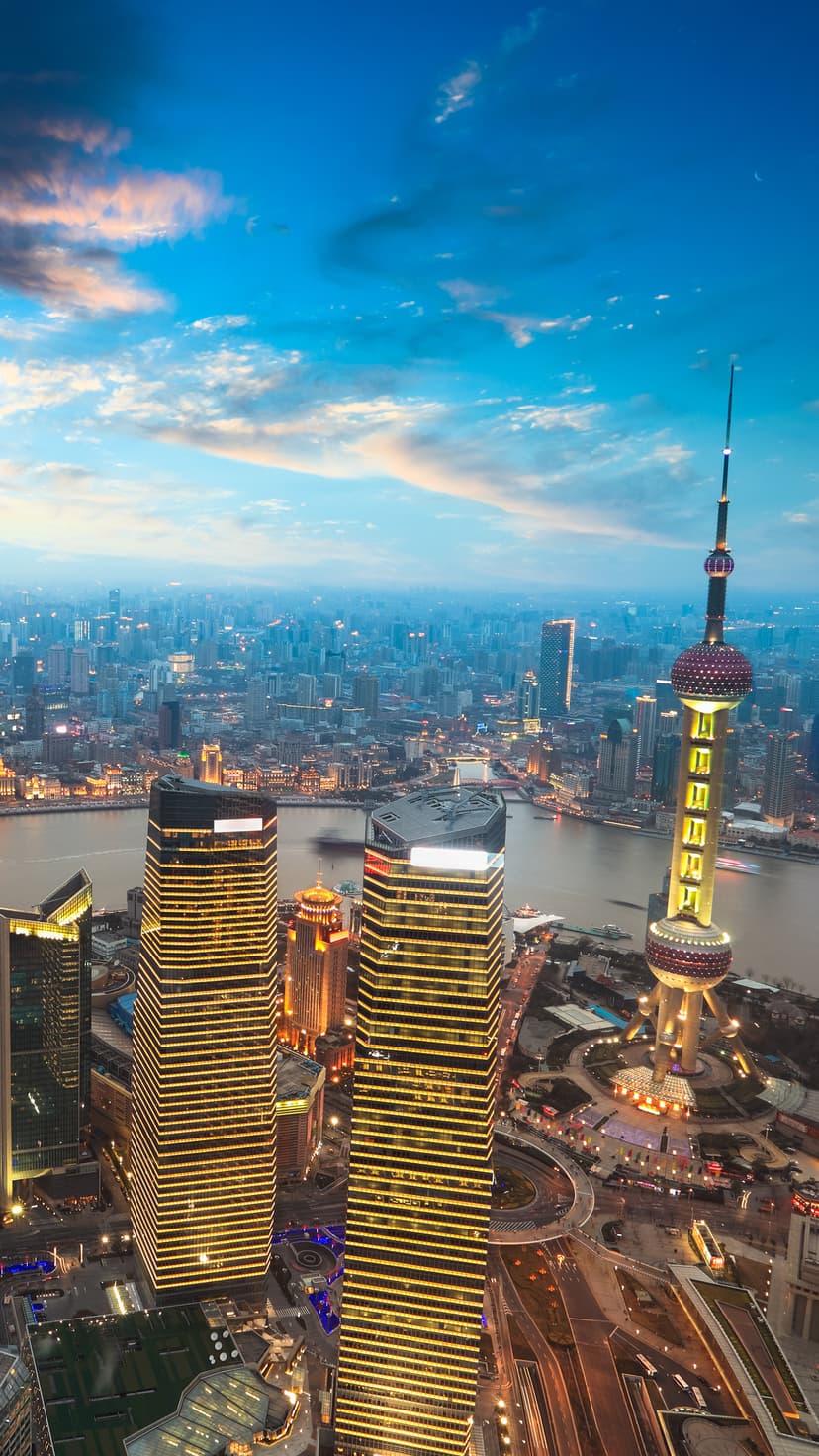 The Oriental Pearl Tower and skyscrapers illuminate the Shanghai skyline along the Huangpu River at twilight.