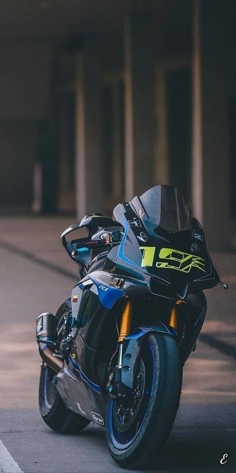 Yamaha R1 motorcycle with blue fairing, yellow 19 decal, and gold front forks against a blurred background.