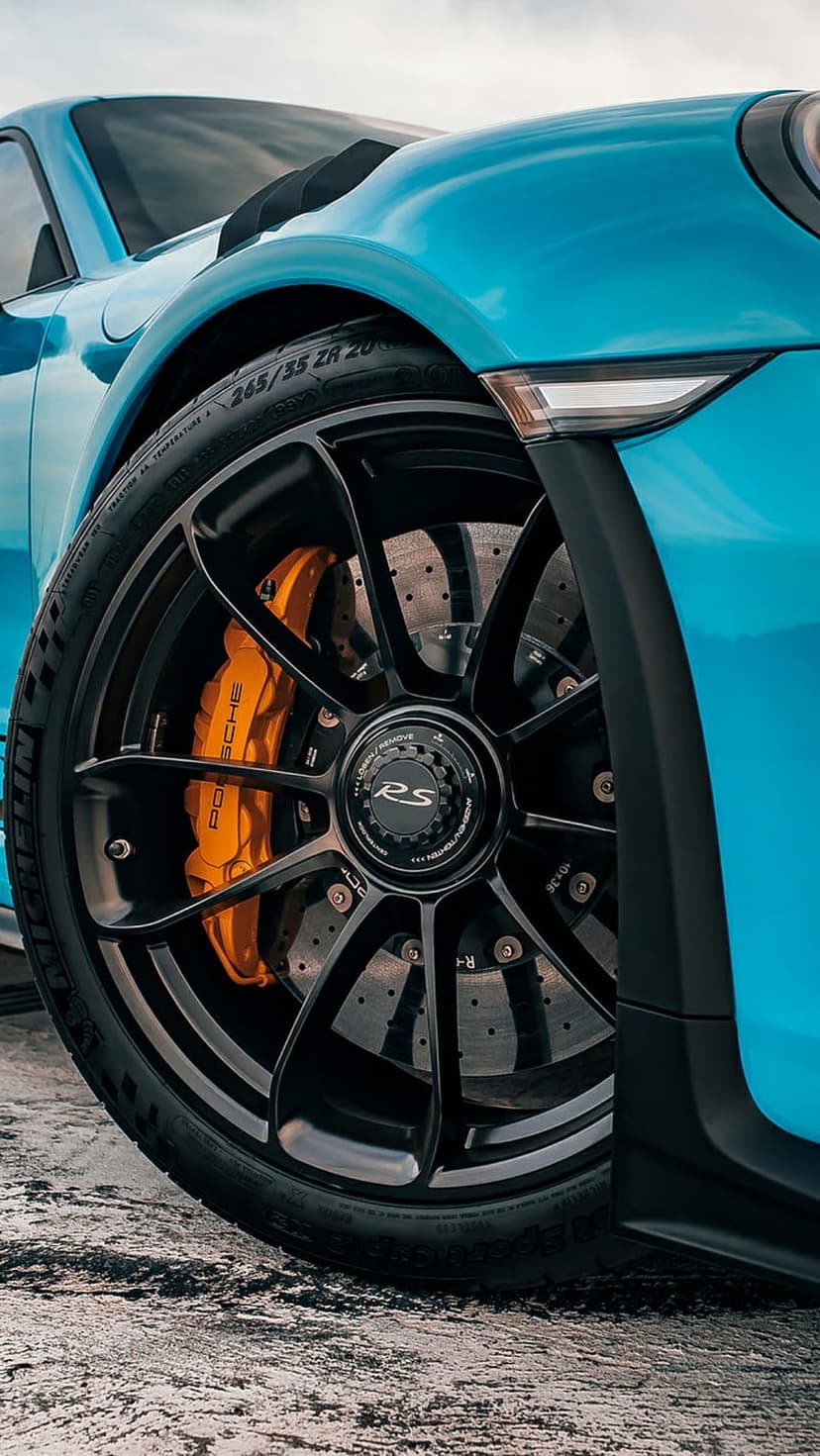 Blue Porsche 911 RS wheel featuring a black rim, orange brake caliper, and ventilated disc on a Michelin tire.