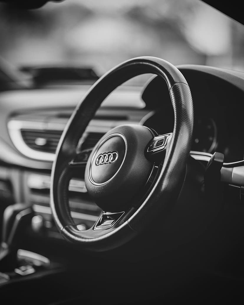 Audi steering wheel emblem and leather texture shown in a close-up black and white vertical automotive shot.