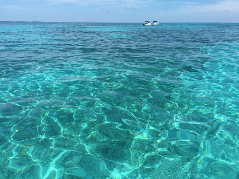 Sunlight reflects on clear turquoise ocean ripples with two small boats floating on the distant blue horizon.