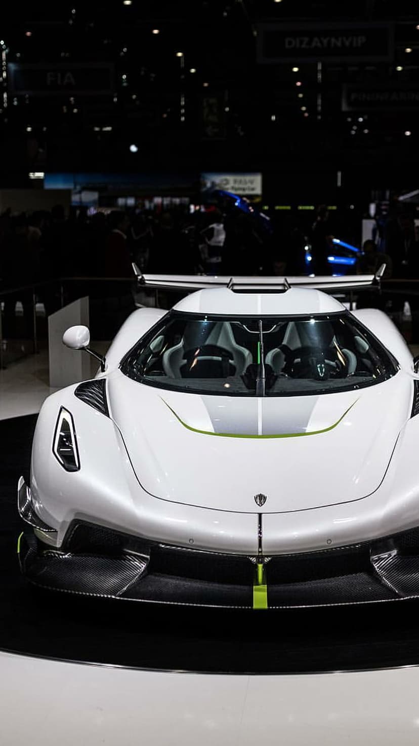 White Koenigsegg hypercar featuring a large rear wing on a dark showroom floor during a luxury automotive event.