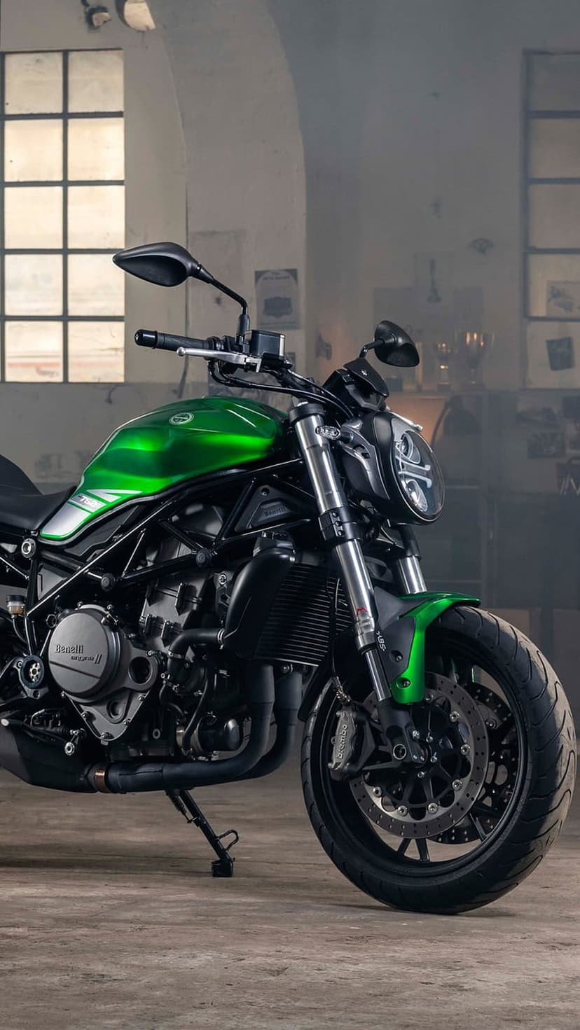 Green Benelli motorcycle with a round headlight parked inside a dimly lit industrial garage with windows.