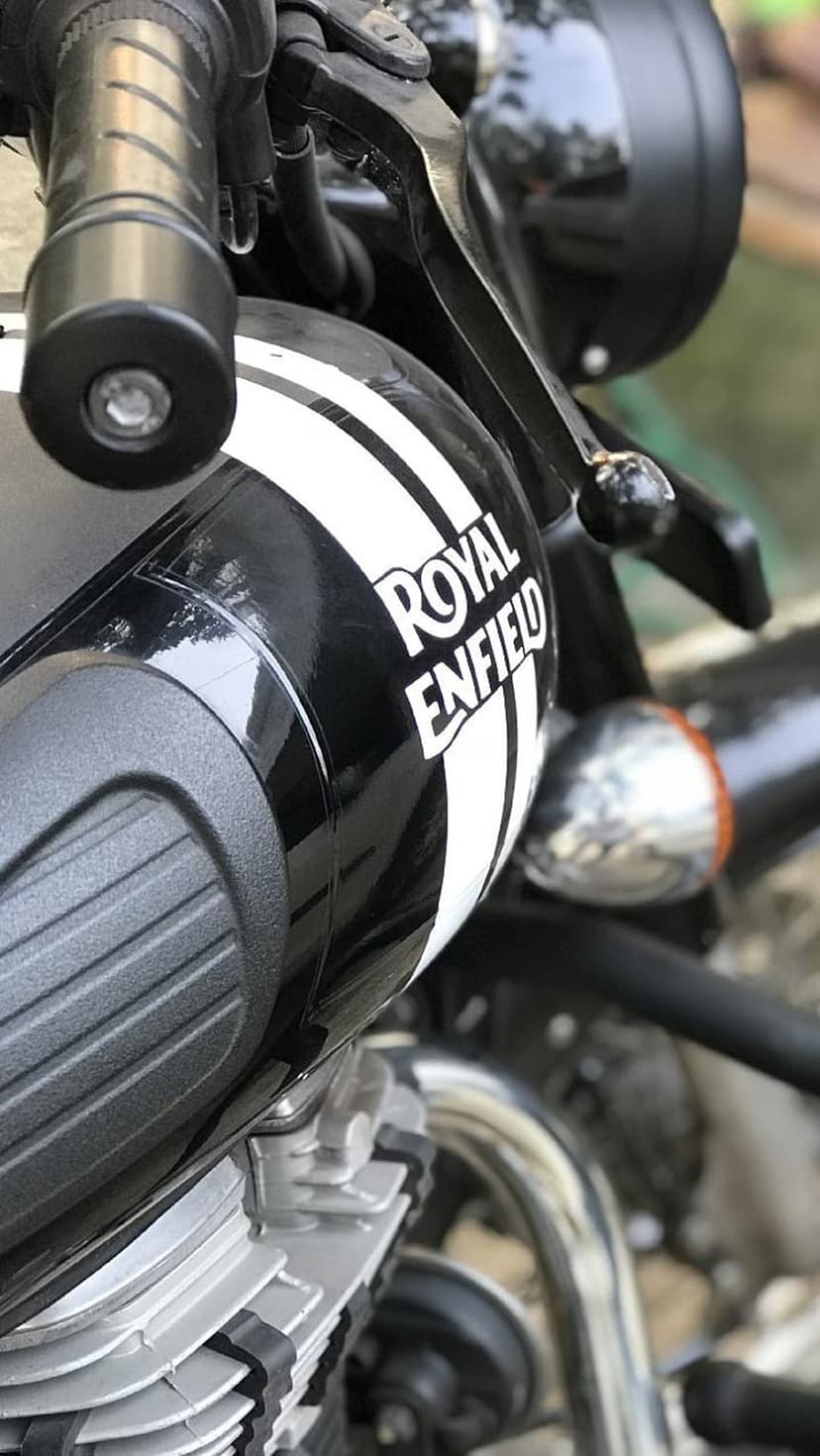 Royal Enfield motorcycle tank with white racing stripes, polished chrome handlebars, and black engine details.