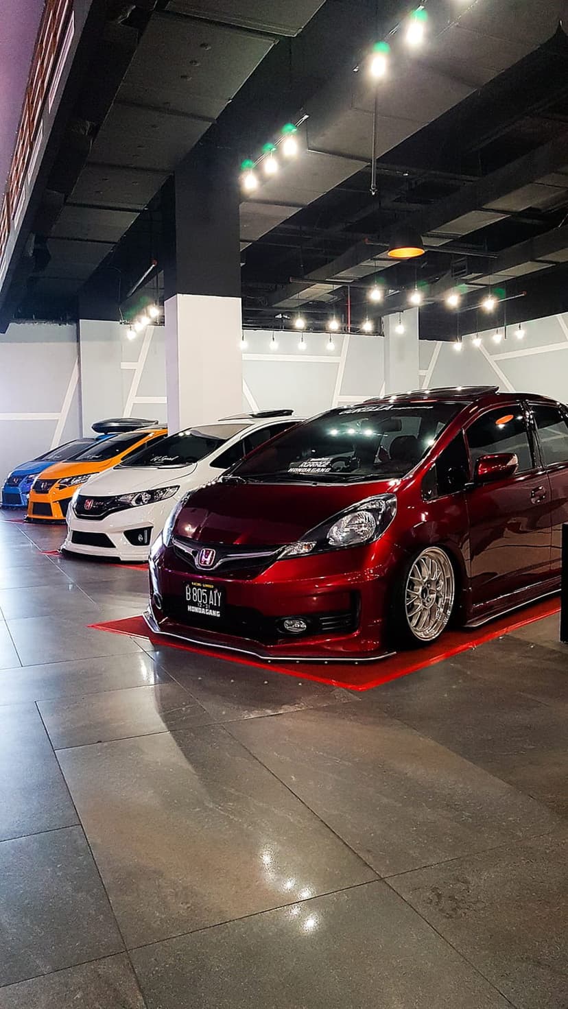 Customized Honda Jazz hatchbacks with lowered stances parked on a reflective showroom floor under soft lighting.