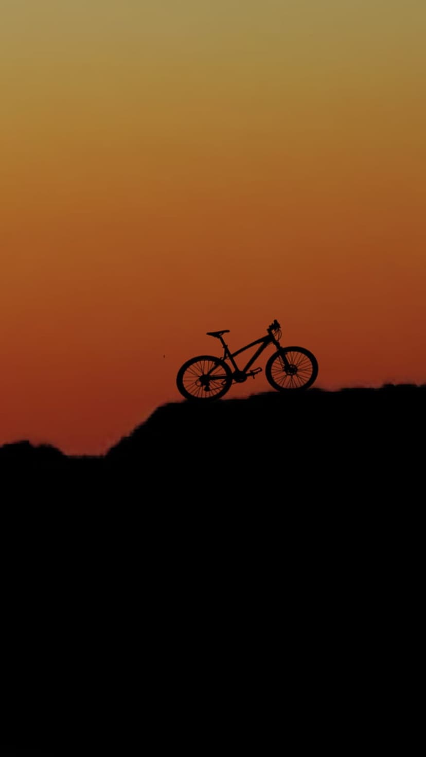 Mountain bike silhouette on a hilltop against a vibrant orange and yellow sunset sky during the golden hour.