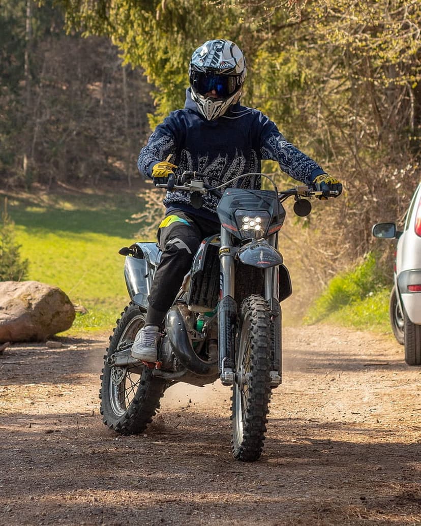 Motocross rider kicking up dust on a forest trail under bright sunlight for a mobile phone screen background.