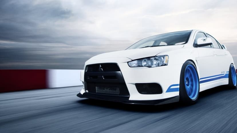 White Mitsubishi Lancer Evolution X with blue wheels racing on a track under a cloudy sky with heavy motion blur.