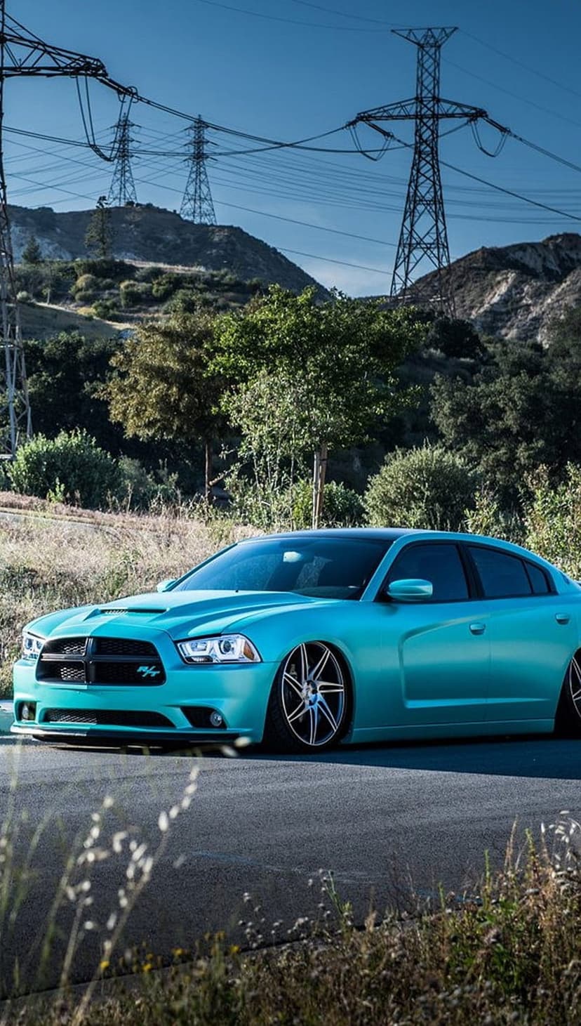 Cyan Dodge Charger with custom wheels on a paved road under power lines and a bright blue sky on a clear day.
