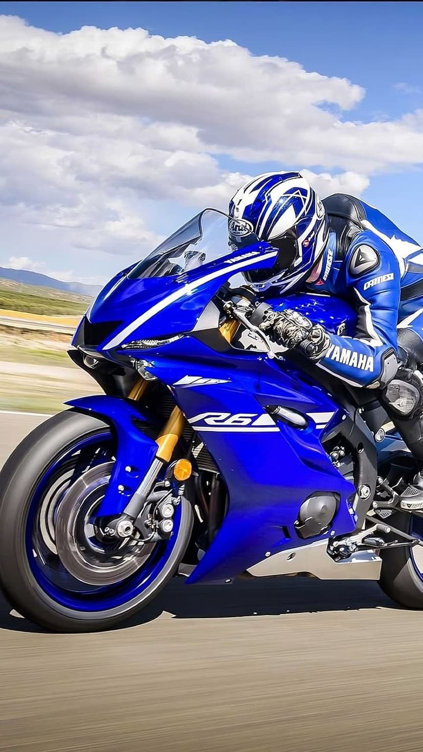 Yamaha R6 rider in blue gear leans through a track corner under a cloudy sky on a high-speed sportbike.