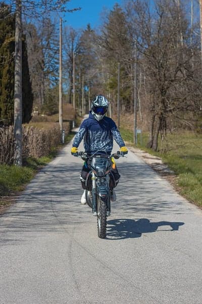 Motorcyclist rides down a tree-lined road on a sunny day
