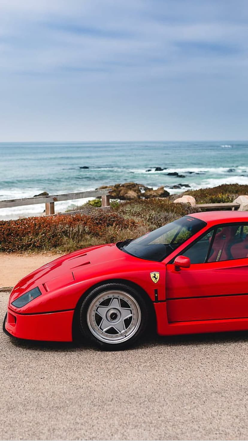 Red Ferrari F40 parked on a seaside highway overlooking jagged cliffs and deep blue ocean water.