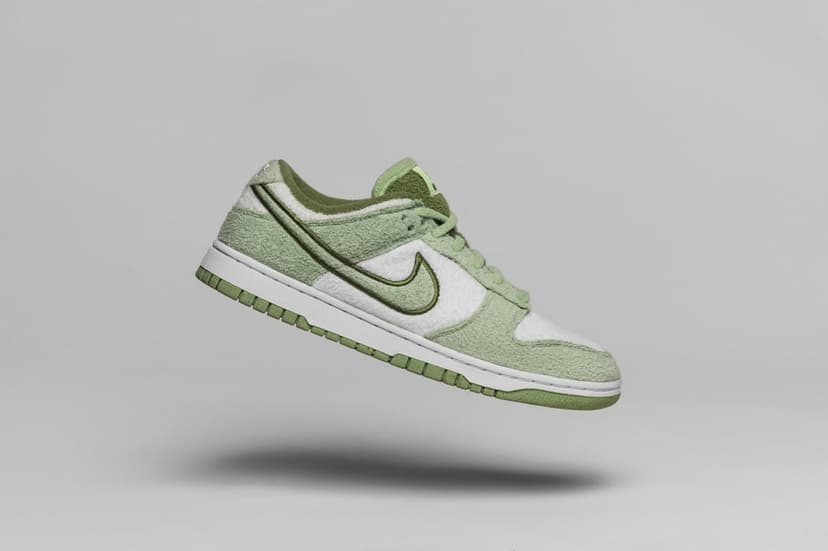 Nike Dunk Low sneakers with green plaid fabric and white leather overlays floating against a gray background.