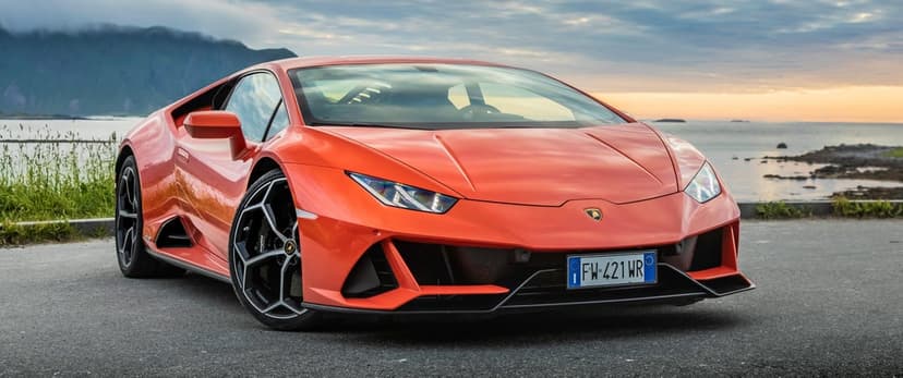 Orange Lamborghini Huracán Evo parked on a coastal road with misty mountains and ocean in the background at dusk.