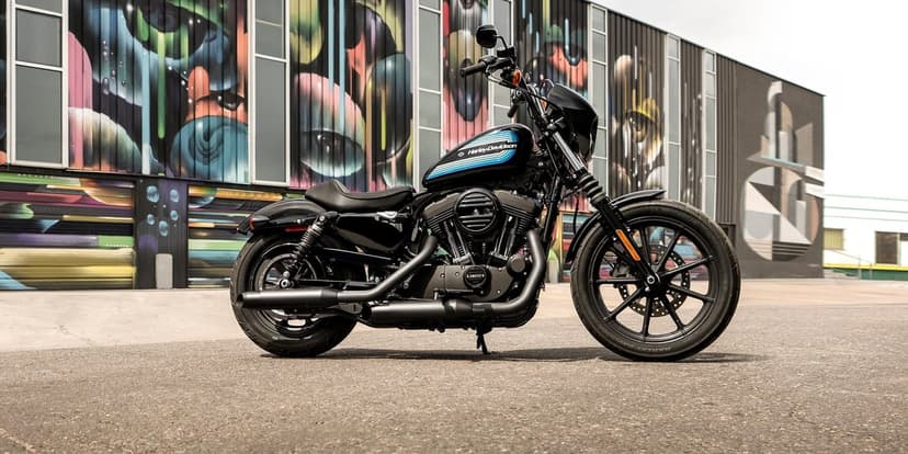 Black Harley-Davidson Iron 1200 motorcycle parked on asphalt in front of a colorful abstract graffiti mural.