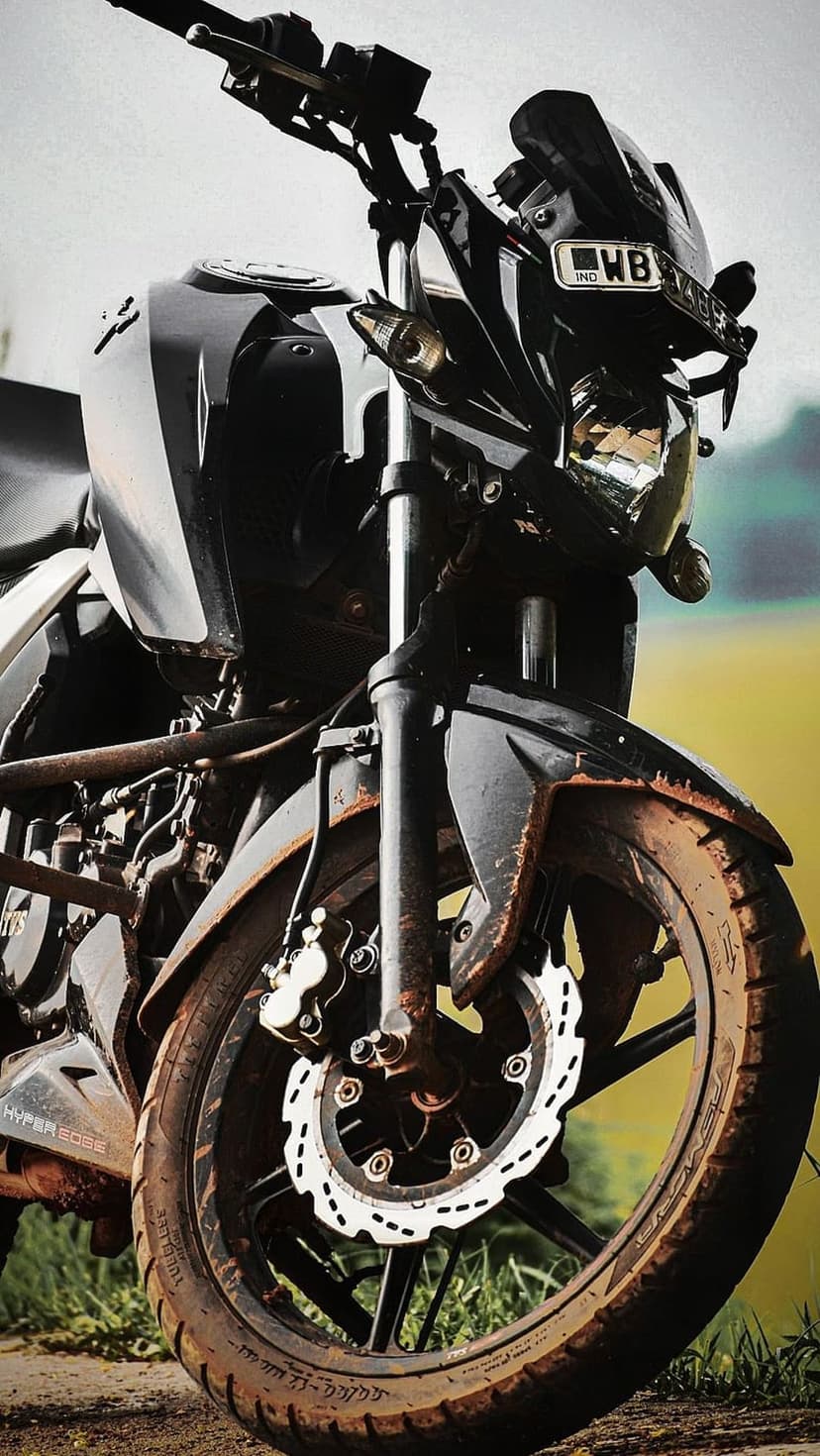 Black motorcycle front tire with muddy treads and handlebars captured in a detailed vertical close-up shot.