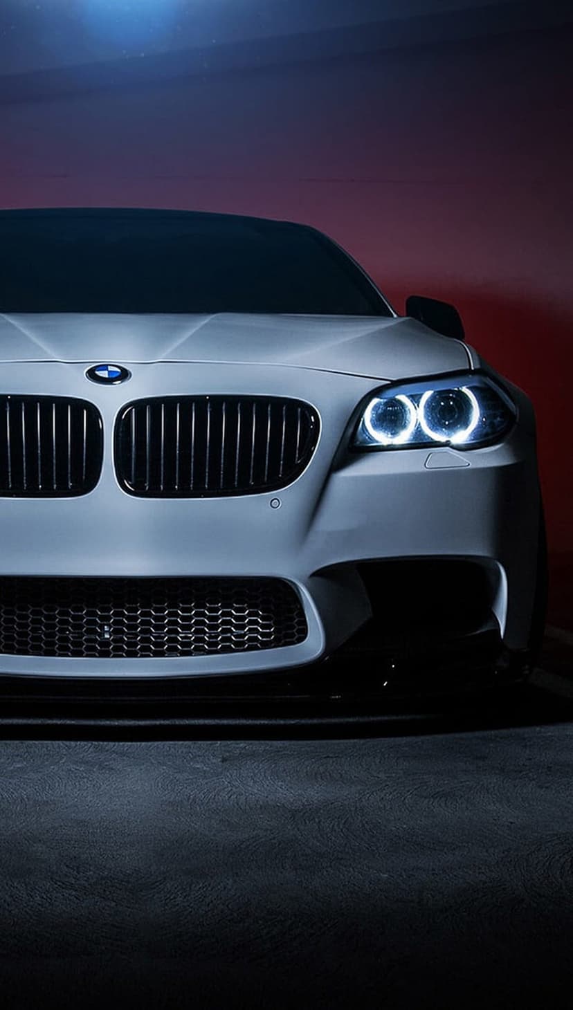 BMW M5 front grille and glowing LED headlights on a white car body with dramatic lighting and dark shadows.