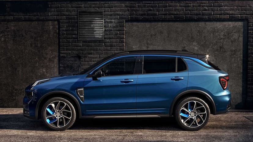 Side profile of a blue metallic SUV with electric blue wheel accents against a dark brick industrial wall.