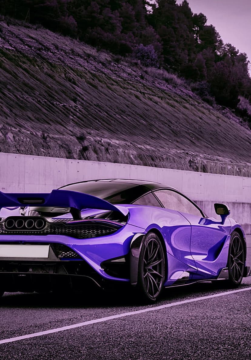 Purple McLaren supercar with a large rear wing and quad exhausts parked on a scenic mountain road during dusk.