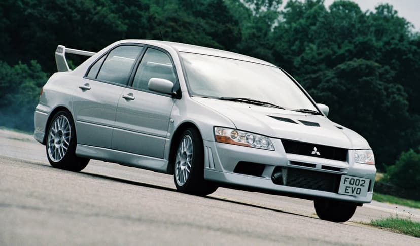 Silver Mitsubishi Lancer Evolution VIII sports car parked on asphalt with a forest background and large rear wing.
