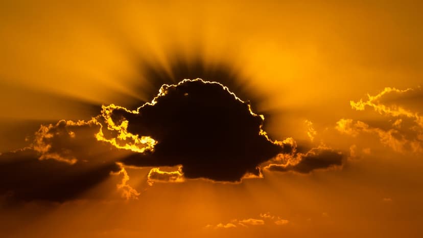 Sunbeams pierce through heavy charcoal clouds against a vibrant orange and golden twilight sky at sunset.