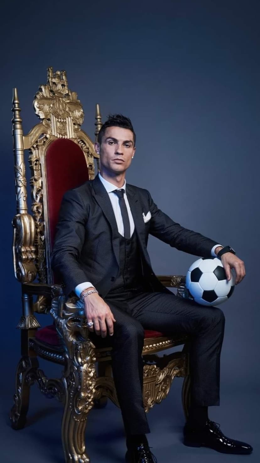 Cristiano Ronaldo in a black suit sits on a golden throne with a soccer ball, portrait orientation.