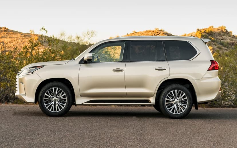 Champagne Lexus LX 570 SUV side profile on a road with golden hills and desert shrubs in the background.
